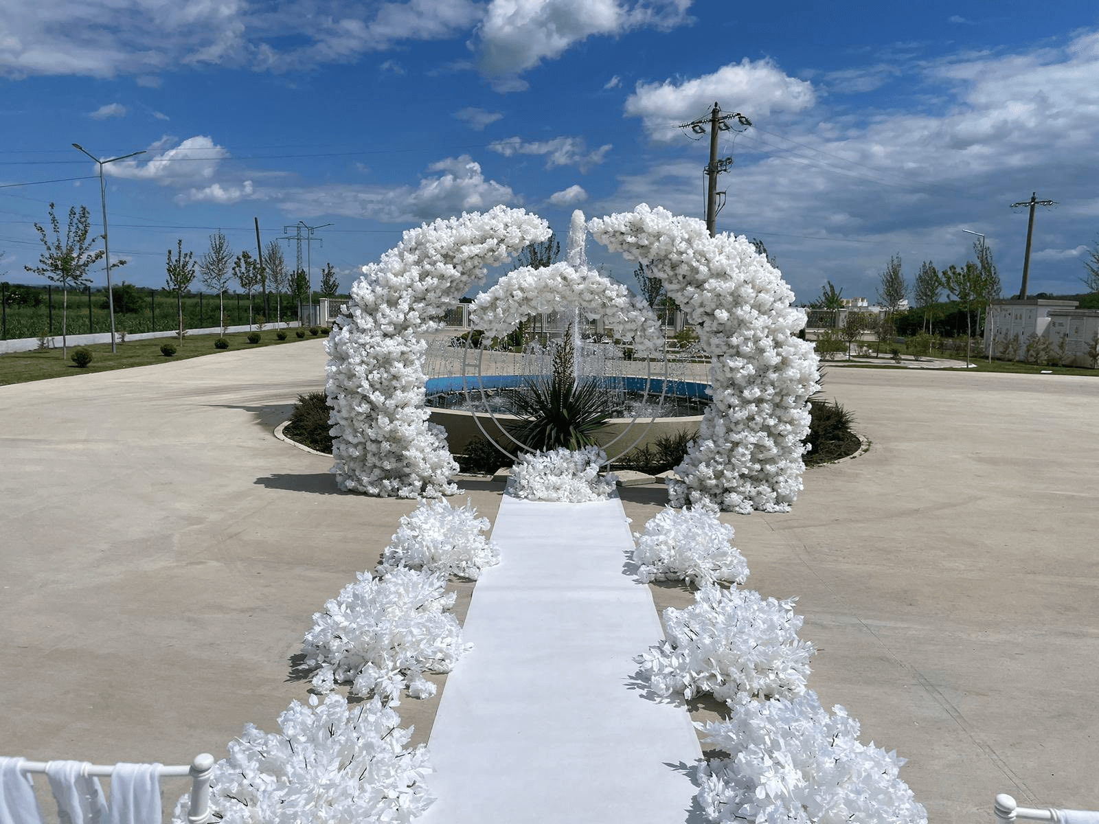 Decor ceremonie civilă în aer liber cu arcade florale albe asimetrice și covor alb flancat de aranjamente tip nori de flori PIM MOOD Events